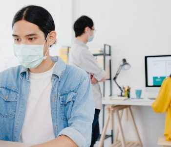 Businessman entrepreneur wearing medical face mask for social distancing in new normal situation for virus prevention while using laptop back at work in office. Lifestyle after corona virus.